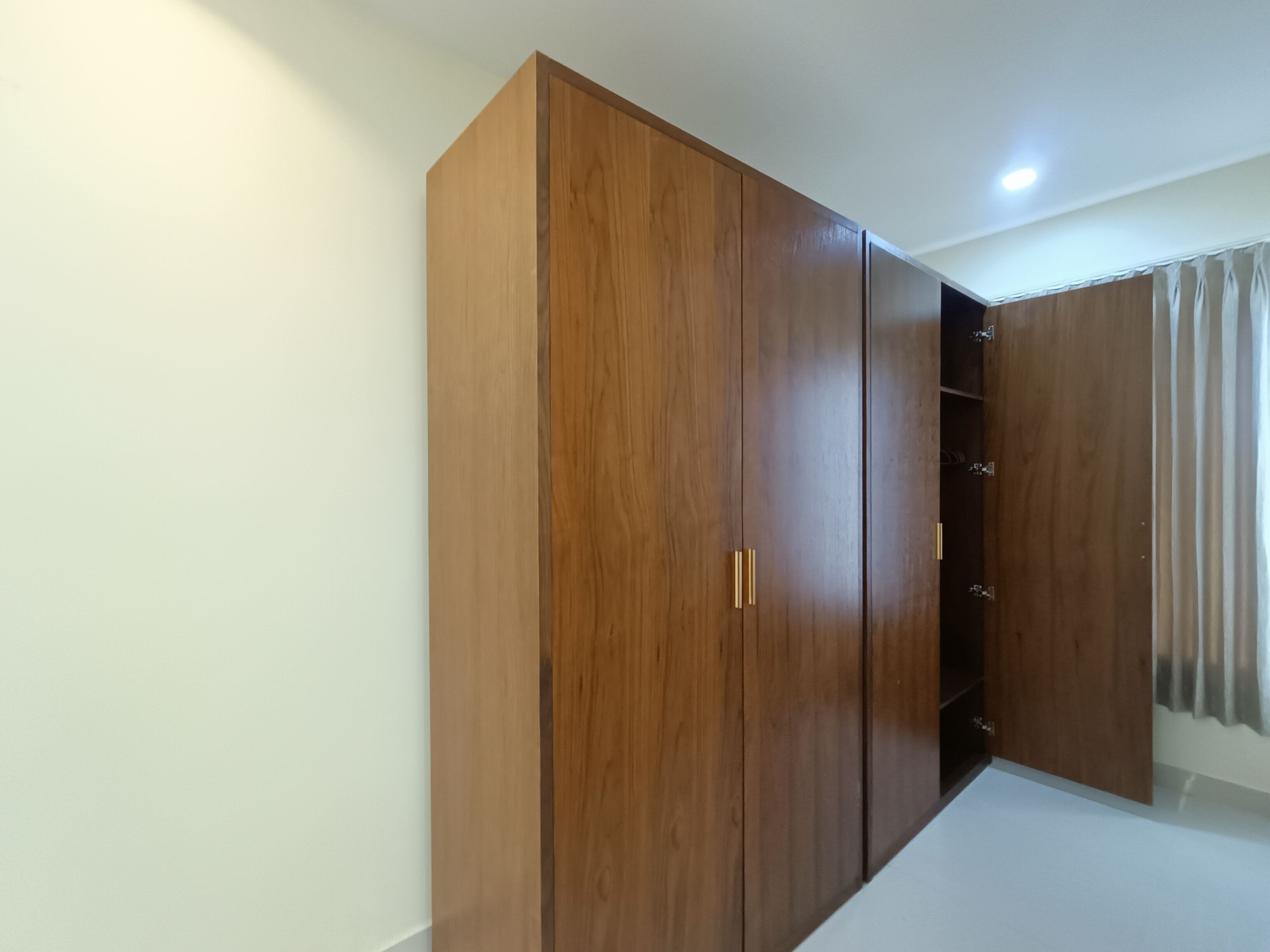 A room with a large wooden wardrobe, a white ceiling, and a curtain on the window.