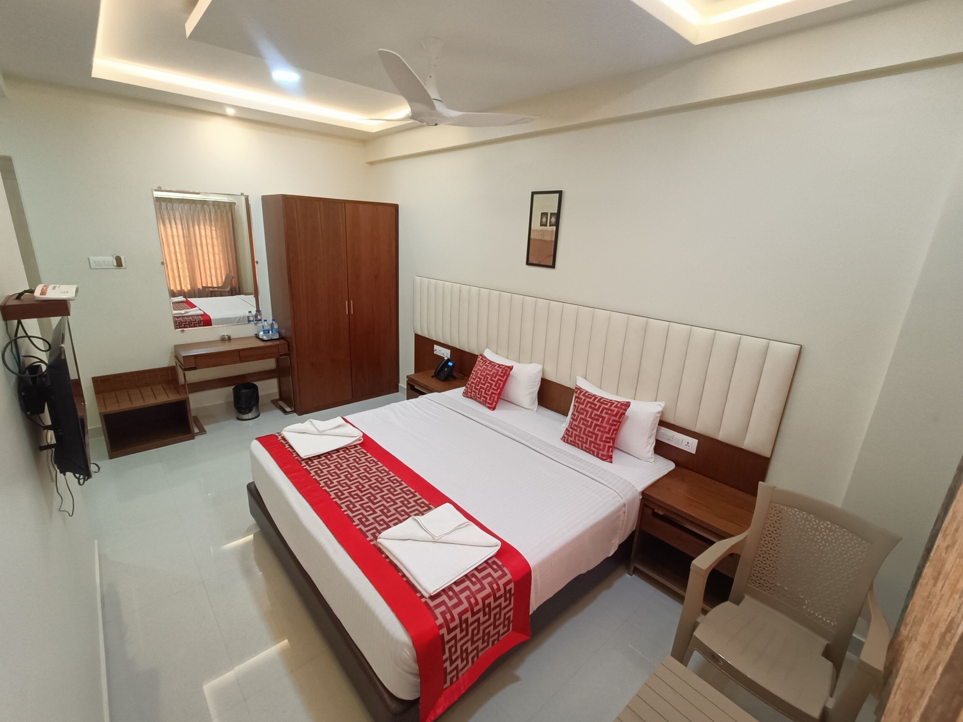 A hotel room with a bed, a desk, a wardrobe, a chair, and a ceiling fan.