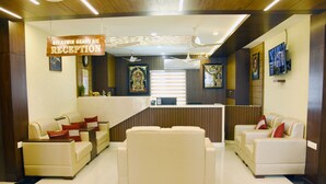 A reception area with a reception desk, two sofas, and a ceiling fan. - Sri Aswin Grand (Namakkal)