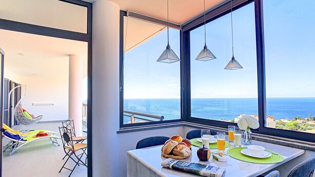Un comedor con una mesa preparada para dos personas, vista al océano y un sillón colgante al fondo.