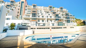 Un moderno edificio residencial de varios pisos con balcones, piscina y cielo azul despejado.