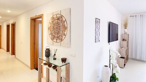 Un pasillo moderno con puertas de madera, una consola de vidrio con objetos decorativos y un cuadro abstracto grande en la pared.