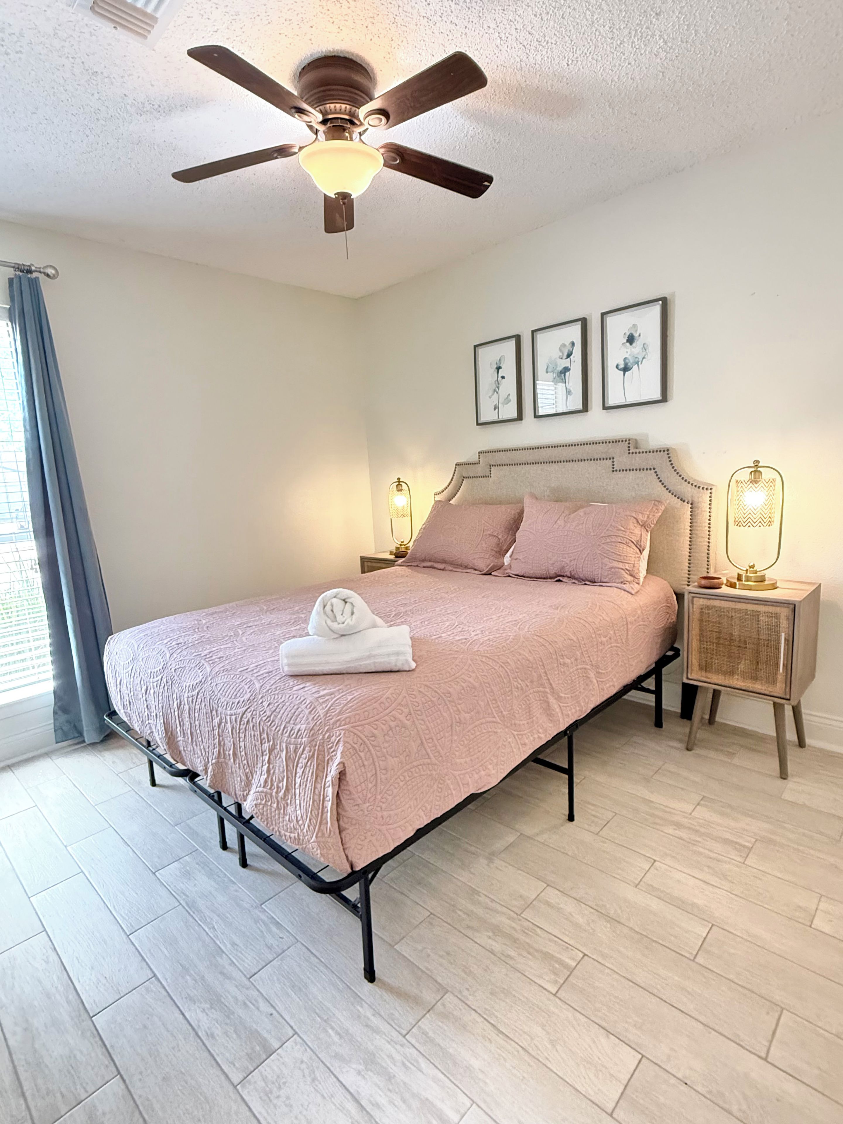 A bedroom with a bed, a ceiling fan, bedside lamps, and framed artwork on the wall.