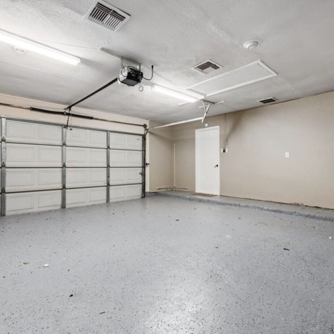 Un garage avec une porte blanche, un ventilateur de plafond et un éclairage fluorescent.