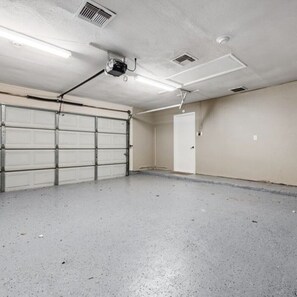 A garage with a white door, a ceiling fan, and fluorescent lighting.