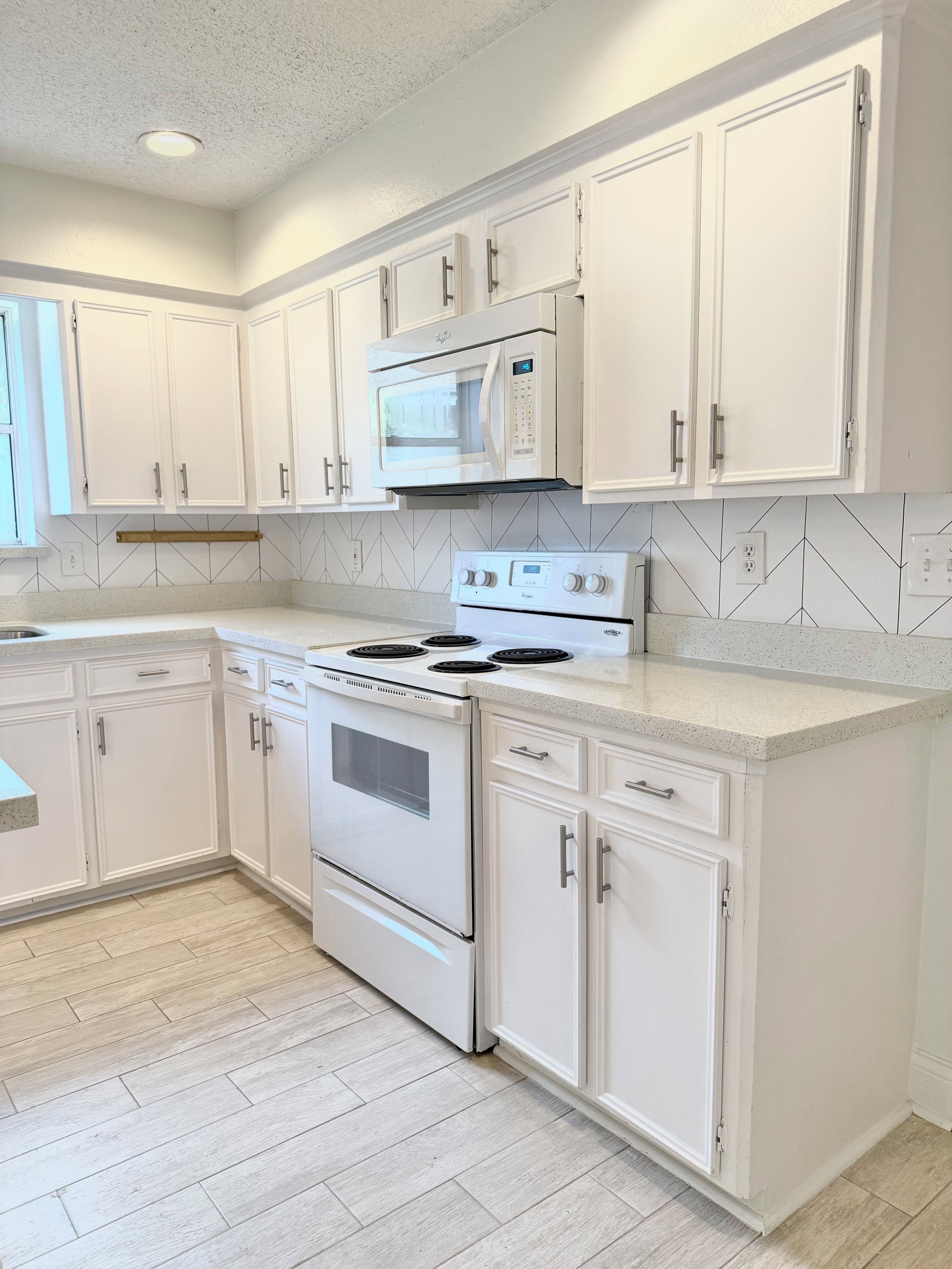 A kitchen with white cabinets, a microwave, a stove, and a tiled backsplash.