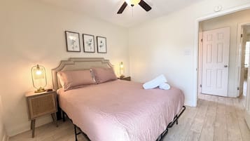 Ein Schlafzimmer mit einem Bett, einem Deckenventilator, einem Nachttisch mit Lampe und einer Tür.