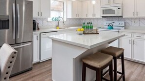 A modern kitchen with white cabinets, stainless steel appliances, and a central island with stools. - Super Cozy Entire House. Close to Everything (Katy)
