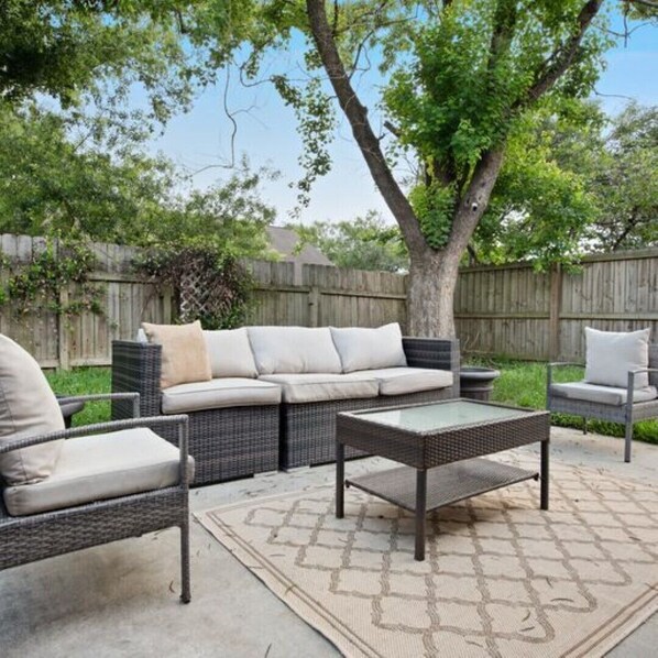 An outdoor patio area with wicker furniture, including a sofa and chairs, a coffee table, and a patterned rug.