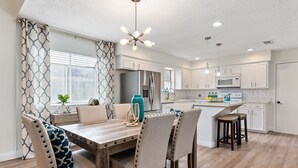 A modern kitchen with white cabinetry, a stainless steel refrigerator, and a central island with stools. - Super Cozy Entire House. Close to Everything (Katy)