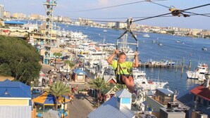 A person zip-lining over a marina with boats and buildings in the background. - Beautiful Gulf & Lake Views | Easy Walk to the Beach and Pool (Miramar Beach)