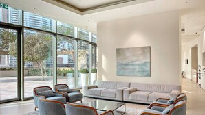 A spacious lobby with a large seating area, a glass coffee table, and a view of the cityscape through large windows.
