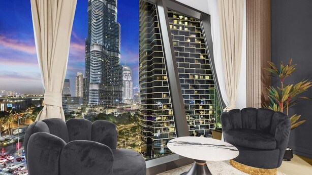 A modern living room with a view of a tall skyscraper, two black armchairs, a round coffee table, and a large window with curtains.