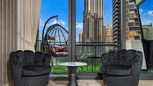 A modern room with two black velvet armchairs, a hanging chair, and a small table. A large window offers a view of a cityscape with tall buildings.