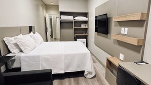Una habitación de hotel con cama, escritorio, silla, televisor y armario.