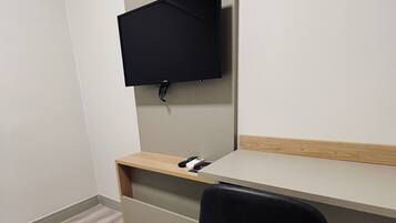A modern hotel room with a wooden desk, a black chair, and a flat-screen TV mounted on the wall.