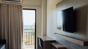 Habitación de hotel con cama, escritorio, televisor, aire acondicionado y balcón con vistas.