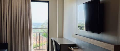 A hotel room with a bed, a desk, a TV, an air conditioner, and a balcony with a view.