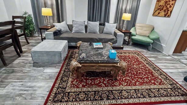 A living room with a sofa, two chairs, a coffee table, a patterned rug, and a painting on the wall. - 115#202 / Charming Downtown Dubuque Apartment (Dubuque)