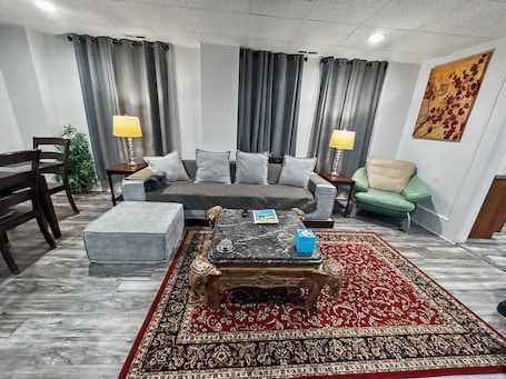 A living room with a sofa, two chairs, a coffee table, a patterned rug, and a painting on the wall.. 115#202 / Charming Downtown Dubuque Apartment