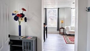 A hallway leading to a living area with a white sofa and a small table with a lamp. - 115#202 / Charming Downtown Dubuque Apartment (Dubuque)