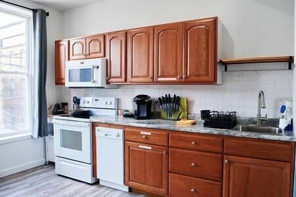 Una cocina con armarios de madera, un microondas, estufa y diferentes utensilios de cocina.