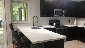 A modern kitchen with a large island, dark cabinets, a microwave, and a kettle.