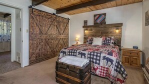 Un dormitorio con una cama grande de madera, un cabecero rústico, una colcha con estampados de animales, un aparador y una puerta de madera.