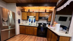 Una cocina con armarios de madera, un refrigerador de acero inoxidable, una estufa negra y piso de madera.