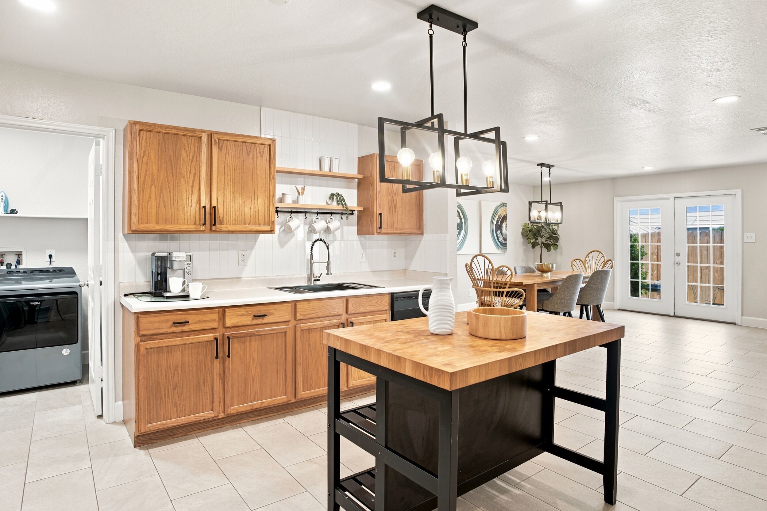 A modern kitchen with wooden cabinets, a built-in oven, a dining area with a table and chairs, and a pendant light fixture.