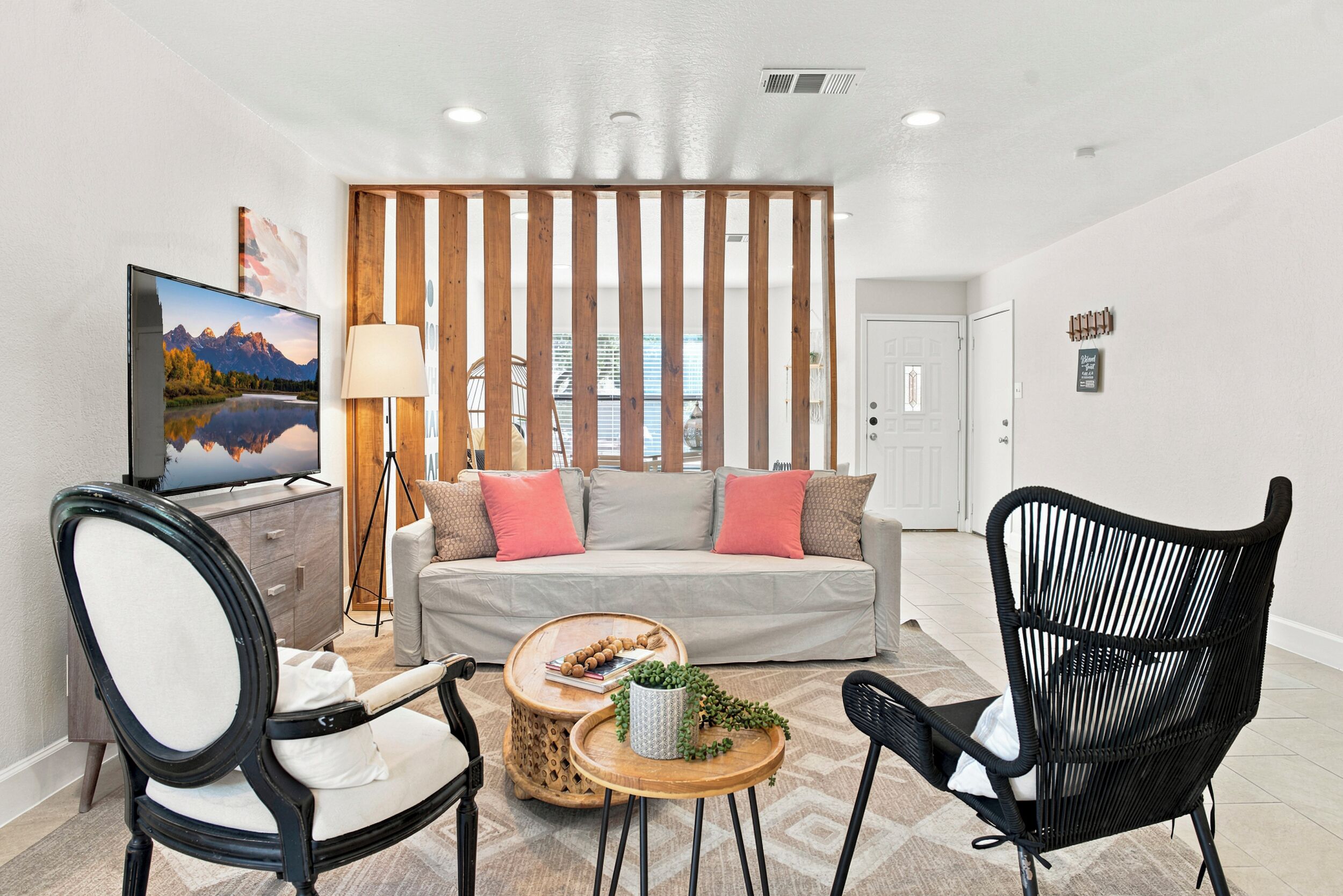 A modern living room with a sofa, two chairs, a coffee table, a TV, and a wooden partition.
