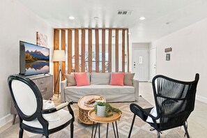 A modern living room with a sofa, two chairs, a coffee table, a TV, and a wooden partition.