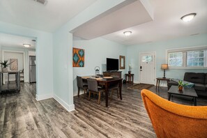 A spacious living area with a dining table, chairs, a sofa, and a TV. - Orchard Beach House Unit #2 (Manistee)