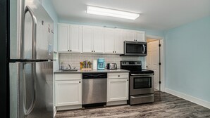 A modern kitchen with white cabinets, stainless steel appliances, and a tiled backsplash. - Orchard Beach House Unit #2 (Manistee)