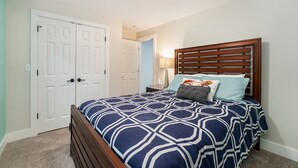 A bedroom with a bed, wooden headboard, and a door with a light switch. - Orchard Beach House Unit #2 (Manistee)