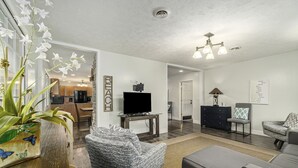 A modern living room with a sofa, armchair, and a television on a stand. - Orchard Beach House Unit #4 (Manistee)