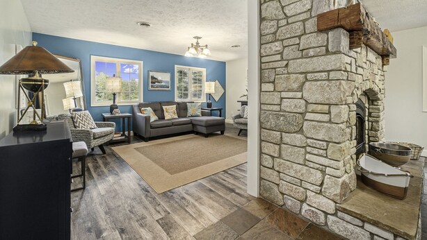 A living room with a stone fireplace, blue walls, and a gray sectional sofa. - Orchard Beach House Unit #4 (Manistee)