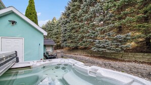 A hot tub area with a stone wall and a building with a door and a window. - Orchard Beach House Unit #4 (Manistee)