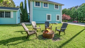 A house with a fire pit and four Adirondack chairs in the front yard. - Orchard Beach House Unit #3 (Manistee)