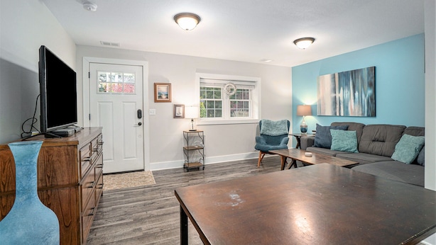 A living room with a wooden coffee table, a sofa, a TV on a wooden cabinet, and a window with a wreath. - Orchard Beach House Unit #3 (Manistee)