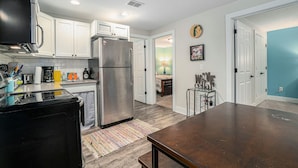 A kitchen with white cabinets, a stainless steel refrigerator, a black stove, and a wooden dining table. - Orchard Beach House Unit #3 (Manistee)