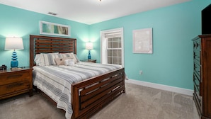 A bedroom with a wooden bed, two bedside tables with lamps, a window, and a dresser. - Orchard Beach House Unit #3 (Manistee)