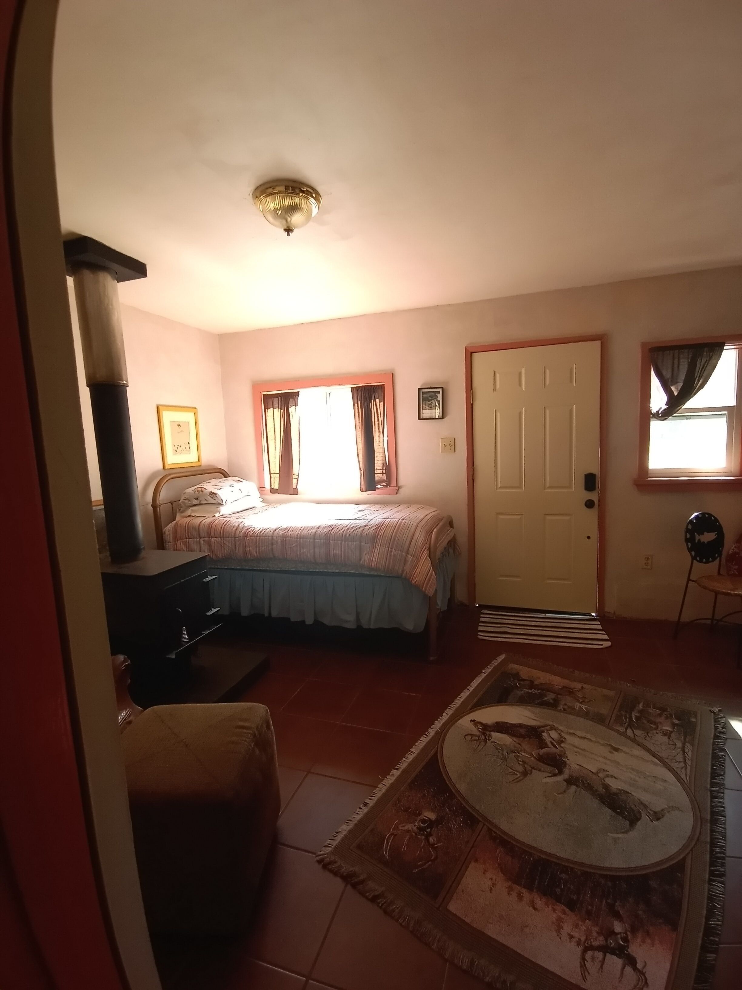 A bedroom with a bed, a desk, a chair, a rug, and a door.