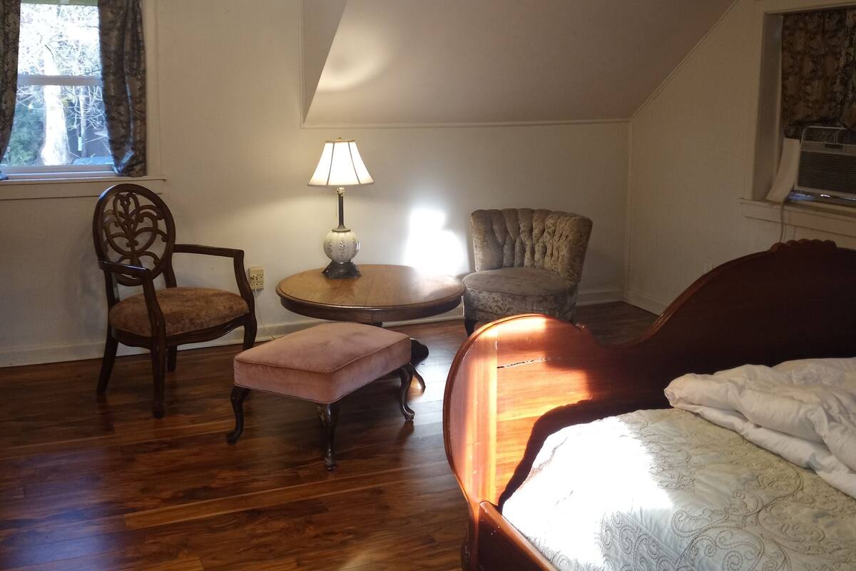 A bedroom with a bed, a chair, a small table, a lamp, and a ceiling fan.