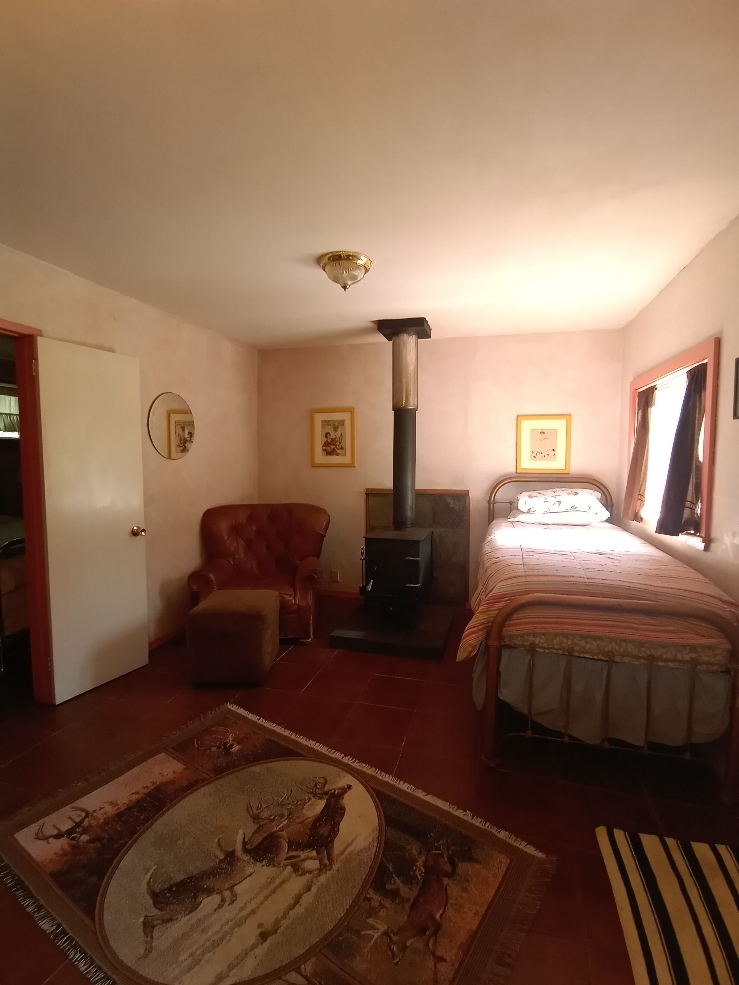 A bedroom with a bed, a chair, a sofa, a fireplace, and a rug with a deer scene.