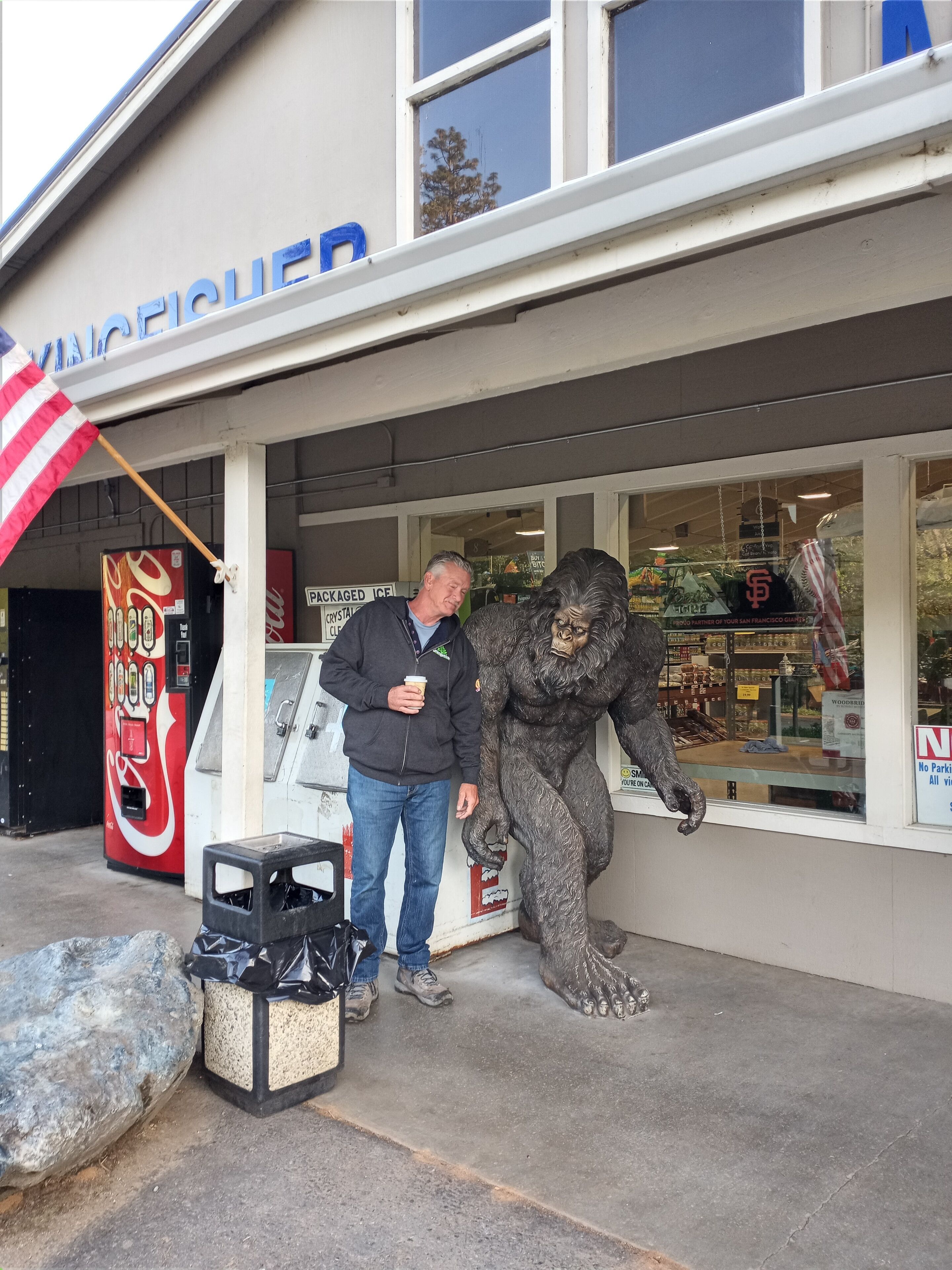 A man standing next to a statue outside a store with a Coca-Cola vending machine and a sign that reads "PACKAGED ICE".