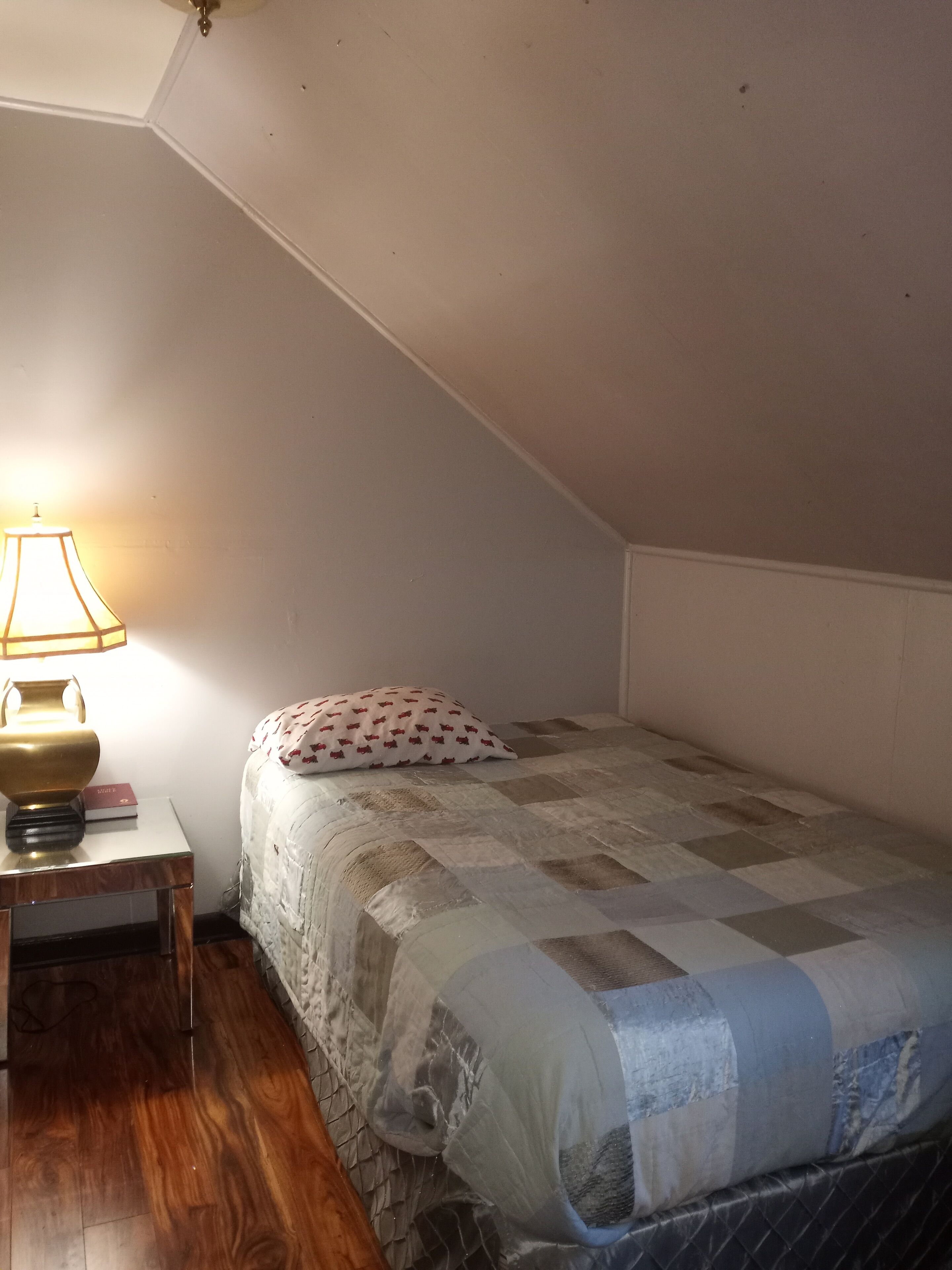 A small, cozy room with a single bed, a nightstand, a lamp, and a ceiling fan.