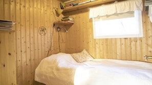Une pièce en bois avec un lit, une fenêtre ornée d’une lambrequin blanche et une étagère contenant des livres et un attrape-rêves.