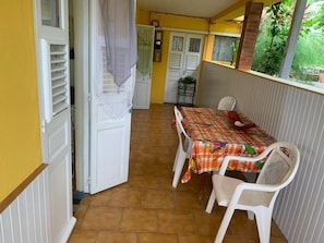 Un petit coin repas avec une table et des chaises, une fenêtre donnant sur un espace verdoyant et une porte menant à une autre pièce.