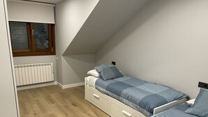 A bedroom with a sloped ceiling, a radiator, and a window with blinds.